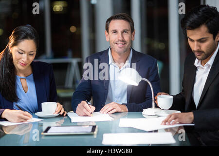 Businessman smiling at camera while colleagues writing on paper Stock Photo