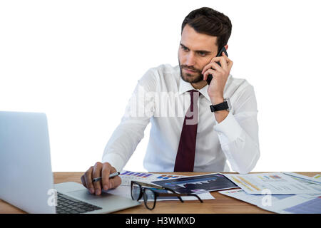Businessman talking on mobile phone while working on laptop Stock Photo