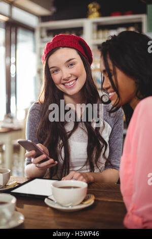 Smiling friends using mobile phone in cafe Stock Photo