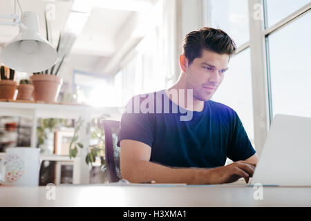 Young businessman using laptop computer in office. Young male executive working on laptop at his desk. Stock Photo