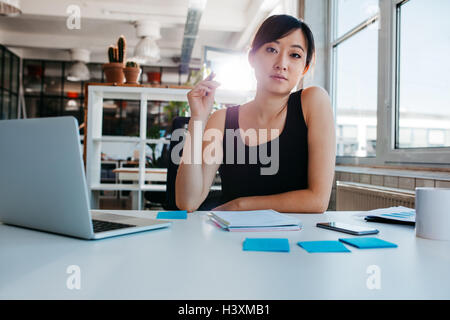 Portrait of confident young woman sitting at her desk with laptop and adhesive notes looking at camera. Asian businesswoman work Stock Photo