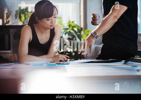 Two young executives discussing new business ideas in office. Colleagues working together on paperwork. Woman sitting at her des Stock Photo