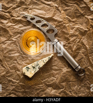 Blue cheese and white dessert wine in glass with knife on crumpled paper. Rustic french food as snack or appetizer. Stock Photo