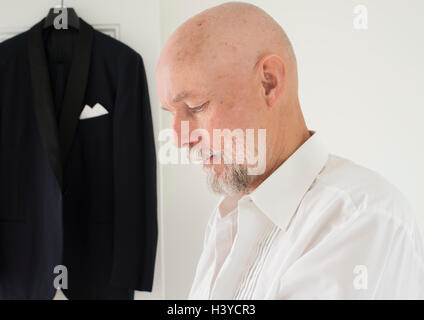 Old man putting on clothes at home, dinner jacket hanging in the background. Lifestyle moment of active retirement. Stock Photo
