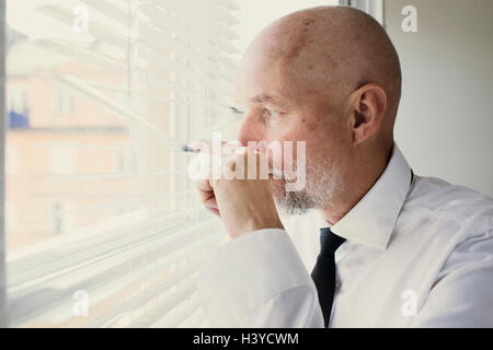 Old man looking out of window through blinds. Concept  of watching and monitoring neighborhood. Feeling insecure in your home. Stock Photo
