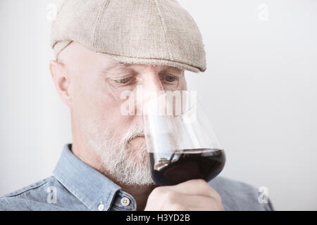 Old man in cap holding wineglass. Smelling the red wine with serious expression. Stock Photo