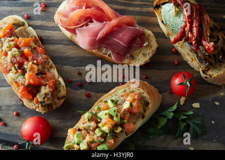 Italian bruschetta with roasted tomatoes, avocado, salmon, ham, peppers, herb Stock Photo