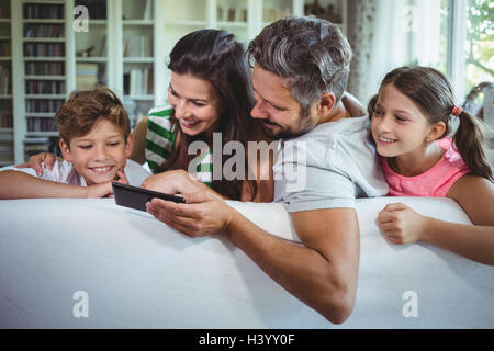 Parents sitting on sofa with their children and using mobile phone in living room Stock Photo