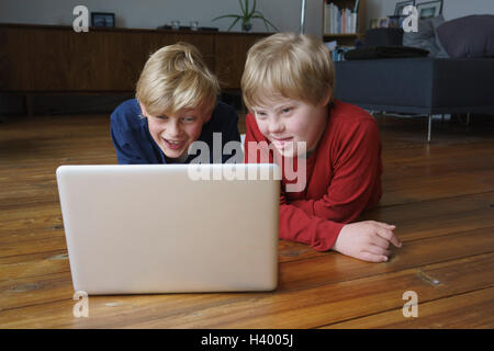 Smiling brothers using laptop while lying on hardwood floor at home Stock Photo