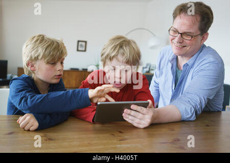 Smiling father with sons using digital tablet at table in house Stock Photo