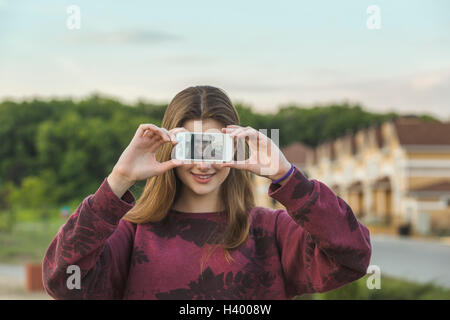 Happy young woman showing display of smart phone with her selfie outdoors Stock Photo