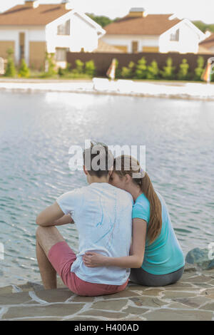Rear view of couple sitting at lakeshore in town Stock Photo