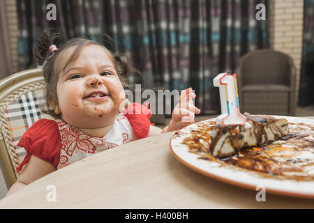 Cute girl with messy face having birthday cake at table Stock Photo