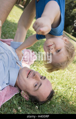 Portrait of father lifting son while lying on grass Stock Photo