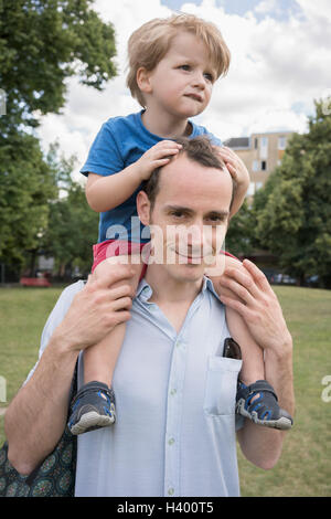 Portrait of father carrying son on shoulders at park Stock Photo