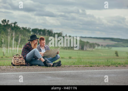 Couple reading map while sitting on roadside against sky Stock Photo