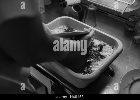 Man washing utensils in trough on kitchen counter Stock Photo