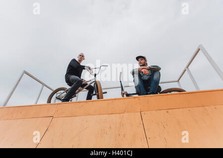 Low angle view of friends with bicycles on ramp against sky Stock Photo