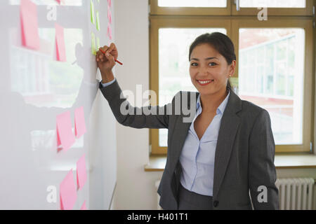 Confident businesswoman writing on adhesive note at creative office Stock Photo