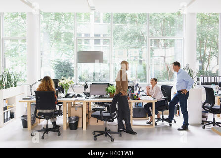Businesswoman working at desk while colleagues discussing in meeting Stock Photo