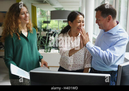 Smiling businesswoman looking at colleagues giving high-five during meeting at office desk Stock Photo