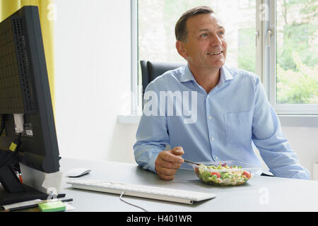 Smiling businessman having salad while sitting at desk in creative office Stock Photo