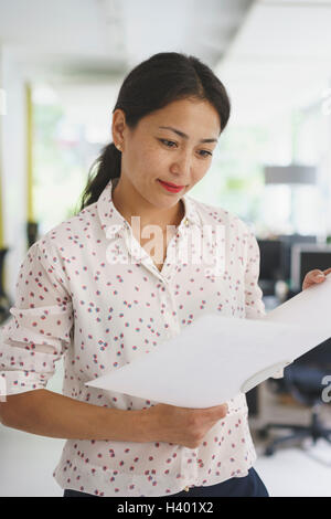 Confident businesswoman reading document while standing at office Stock Photo