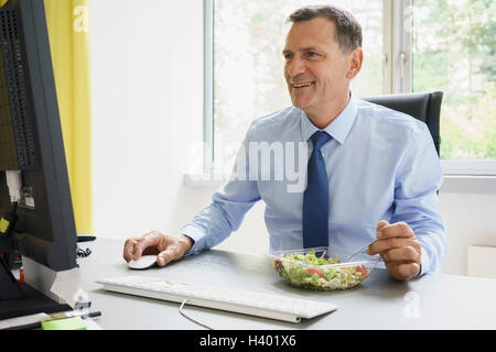 Smiling businessman working on computer while having salad at desk in creative office Stock Photo