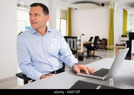 Smiling businessman working on laptop at desk in creative office Stock Photo