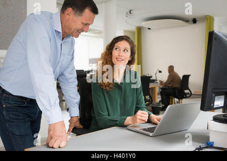 Happy business colleagues discussing over laptop at office desk Stock Photo