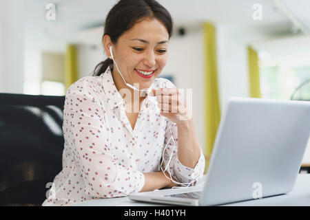 Smiling businesswoman using headphones and laptop at office desk Stock Photo