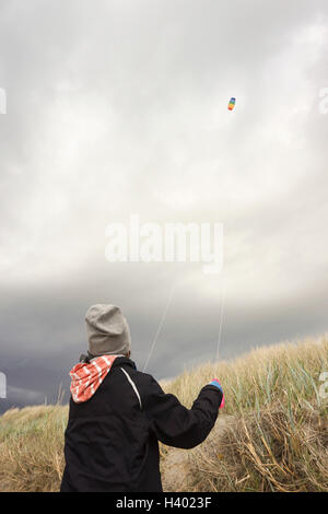Rear view of boy flying kite against cloudy sky Stock Photo