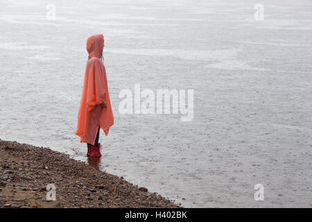Woman wearing raincoat standing at lakeshore during rainy season Stock Photo