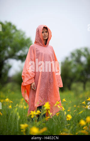 Woman wearing raincoat standing amidst yellow flowering plants in rainy season Stock Photo
