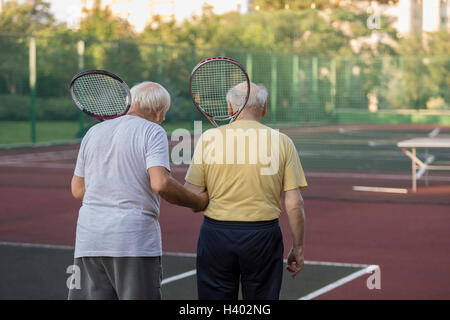 Rear view of senior friends carrying tennis rackets while walking at playing field Stock Photo