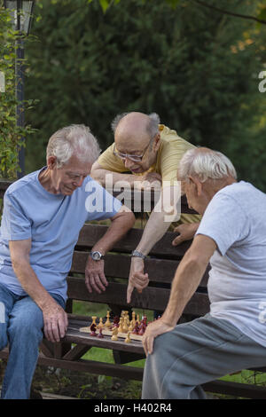 Senior man guiding friends in playing chess at park Stock Photo