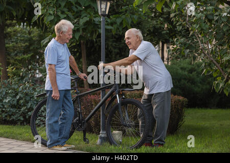 Smiling friends talking while standing by bicycle on field at park Stock Photo