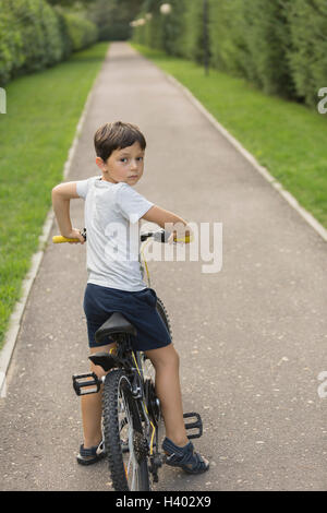 Cute boy cycling on road amidst grassy field in park Stock Photo