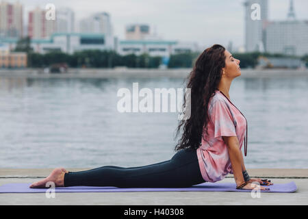 Side view of woman practicing yoga in cobra pose by river at city Stock Photo