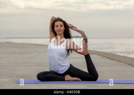Beautiful woman practicing yoga in mermaid pose at beach Stock Photo