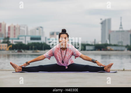 Beautiful woman practicing yoga against river in city Stock Photo