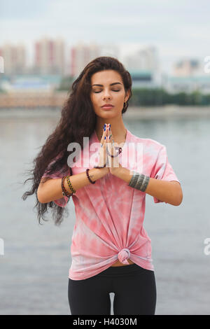 Young woman with closed eyes practicing yoga in prayer position against river
