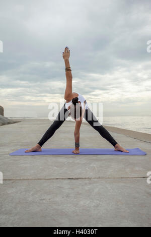 Woman practicing yoga at beach against cloudy sky Stock Photo