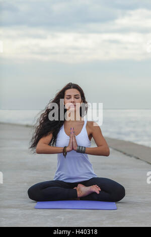 Woman with closed eyes practicing yoga in prayer position at beach against cloudy sky Stock Photo