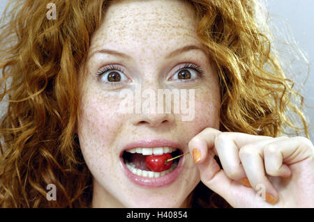 Woman, cherry nibble, facial play, caught, portrait, women's portrait, redheads, red-haired, curls, look, expression, surprises, surprise, fruit, fruit, eat, nutrition, healthy, vitamins, rich in vitamins, intermeal Stock Photo