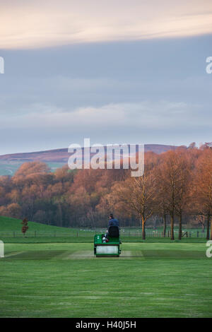 Man driving a ride-on roller, preparing the wicket of a village cricket pitch - Bolton Abbey Cricket Club, Yorkshire Dales.