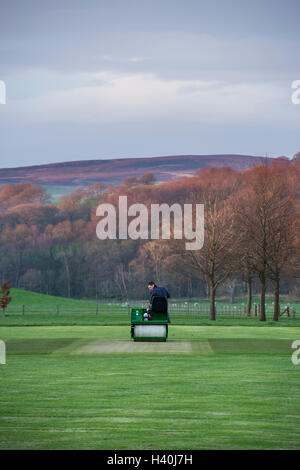 Man driving a ride-on roller, preparing the wicket of a village cricket pitch - Bolton Abbey Cricket Club, Yorkshire Dales.
