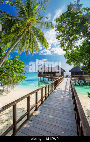 Bridge leading to overwater bungalow in blue lagoon around tropical island Stock Photo