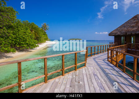 Bridge leading to overwater bungalow in blue lagoon around tropical island Stock Photo