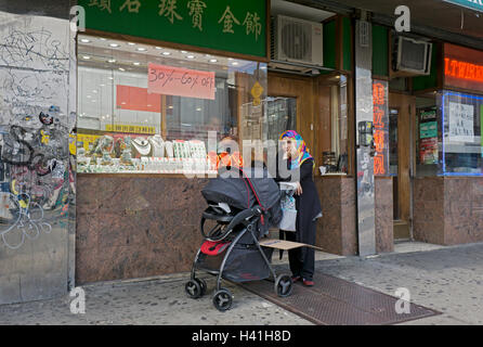 A Muslim woman lost in her thoughts with a baby carriage outside a jewelry store on Roosevelt Ave. in Downtown Flushing, Queens. Stock Photo